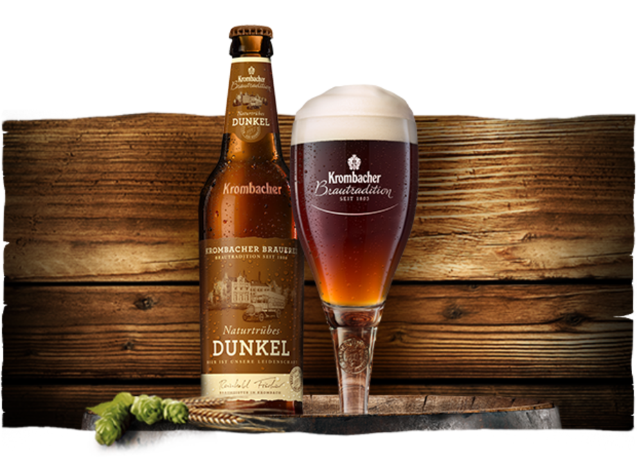 Eine Flasche Krombacher Dunkel Bier steht neben einem Glas mit schaumigem Bier. Im Hintergrund ist eine Holzoberfläche sichtbar.