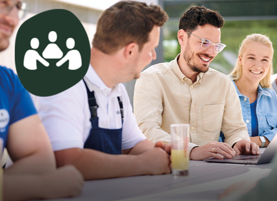 Mehrere Personen sitzen an einem Tisch vor einem Laptop und lächeln, Headline: 'Gemeinsam wachsen liegt in unserer Natur'.