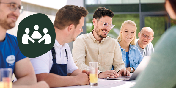 Mehrere Personen sitzen an einem Tisch vor einem Laptop und lächeln, Headline: 'Gemeinsam wachsen liegt in unserer Natur'.