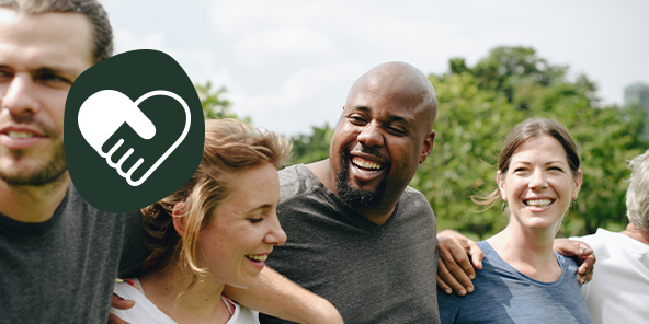 Vier Menschen stehen aneinandergereiht nebeneinander und legen sich die Arme über die Schultern, alle lächeln. 