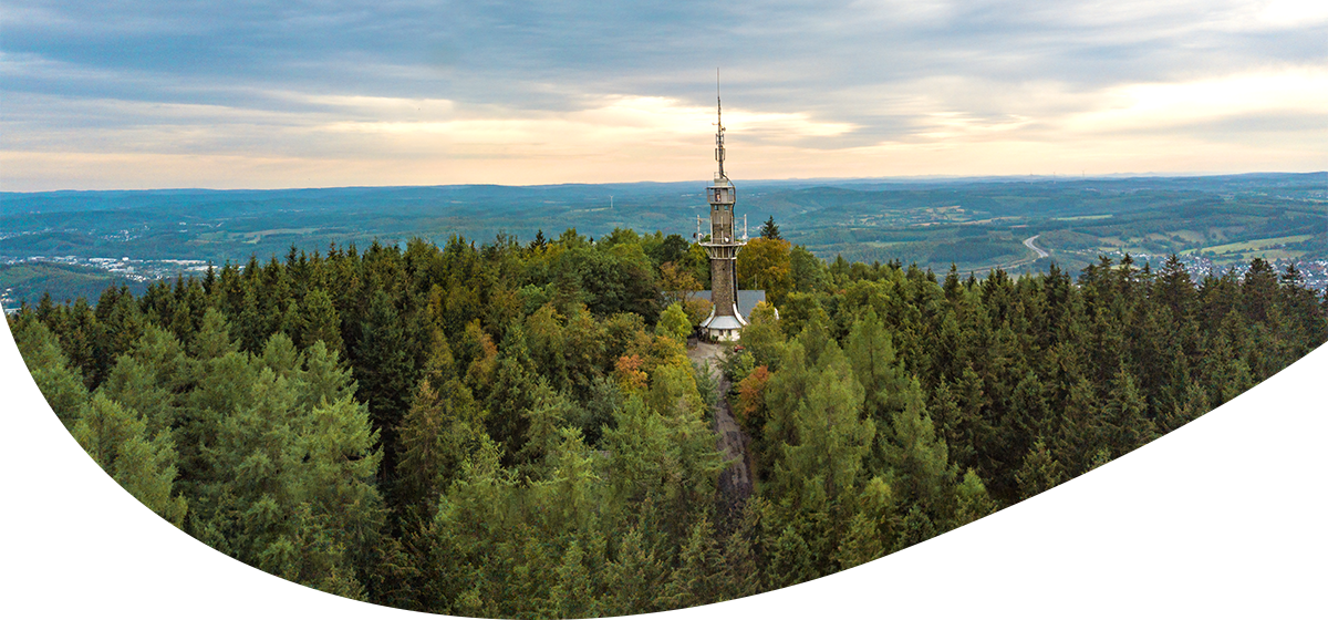 Fernblick auf einen den Kindelsturm in Kreuztal, inmitten eines dichten Nadelwalds unter bewölktem Himmel.