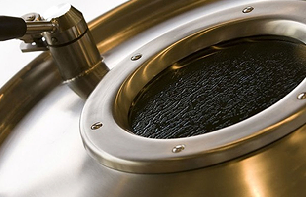 Nahaufnahme eines metallischen Gärkessels mit rundem Deckel und schwarzem Inhalt.