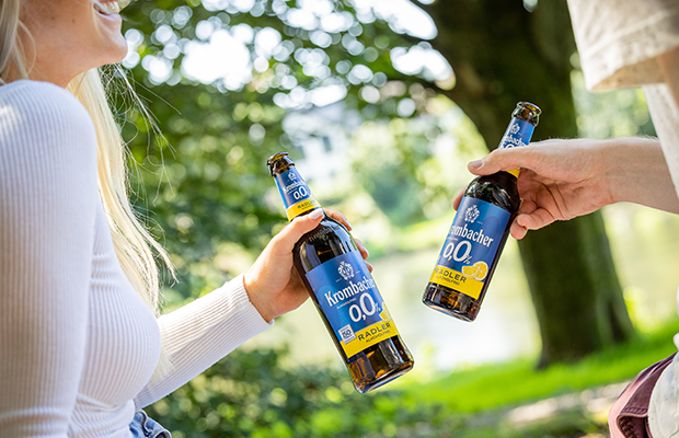 Zwei Personen stoßen im Freien mit Krombacher o,0% Radler an.