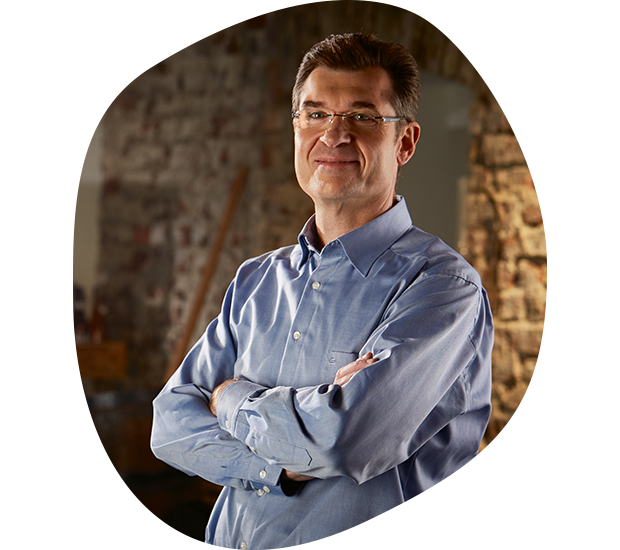 Auf dem Bild ist Manfred Schmidt, Geschäftsführer der Produktion und Technik. Er trägt ein blaues Hemd, hat kurze Braune Haare, eine Brille und lächelt.