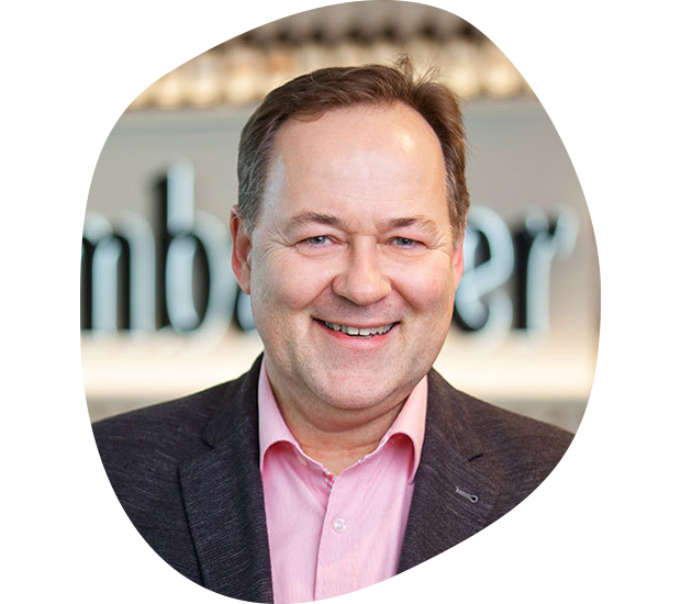 Portrait von Andreas Scholten, Leiter Produktmanagement. Er hat hellbraune Haare und trägt ein rosa Hemd mit einem dunkelgrauen Anzug.