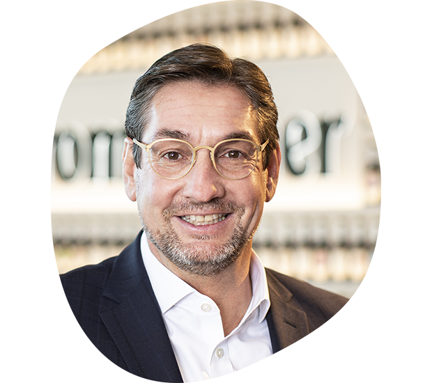 Volker Arens, Head of People & Culture, hat grau-braune Haare, lächelt und trägt eine Brille. Er hat ein weißes Hemd mit einem schwarzen Anzug an.