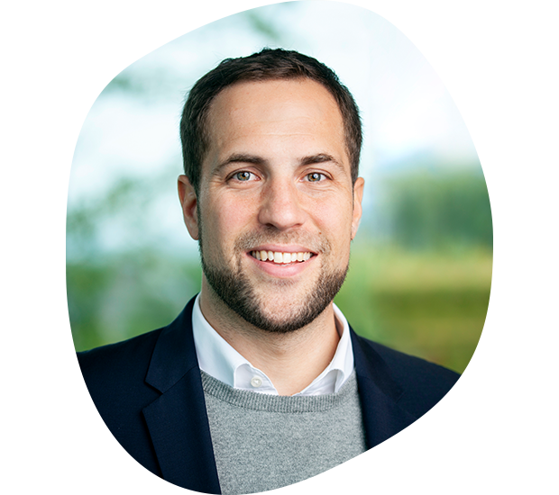 Portrait von Peter Lemm, Leiter Unternehmenskommunikation. Er hat braune Haare, lächelt und trägt einen hellgrauen Pullover unter einem dunkelblauen Anzug.