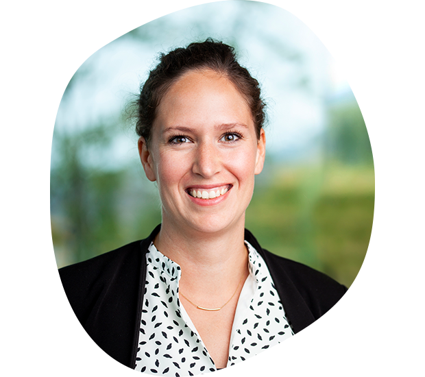 Auf dem Bild ist Pia Munschek-Jung, Abteilungsleiterin für Unternehmenskommunikation lächelt. Sie hat dunkle, zurückgebundene Haare, trägt eine schwarze Jacke und weiße Bluse mit schwarzen Punkten. 