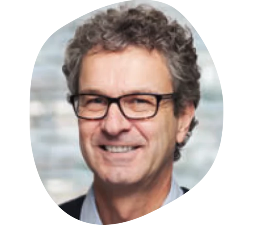 Mann mit lockigem braun-grauem Haar, trägt Hemd und dunkles Sakko.