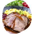 Zwei Scheiben Braten mit brauner Soße, dazu Spätzle, Preiselbeeren und frische Kräuter auf dunklem Teller.