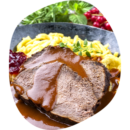 Zwei Scheiben Braten mit brauner Soße, dazu Spätzle, Preiselbeeren und frische Kräuter auf dunklem Teller.