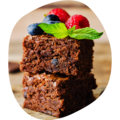 Zwei übereinander gestapelte quadratische Schokoladenbrownies mit Blaubeeren, Himbeeren und Minzblatt als Dekoration.