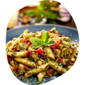 Teller mit Penne-Pasta, Pesto, getrockneten Tomaten, Kräutern und Basilikumblättern als Garnitur.