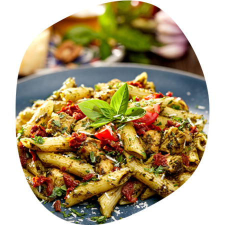 Teller mit Penne-Pasta, Pesto, getrockneten Tomaten, Kräutern und Basilikumblättern als Garnitur.