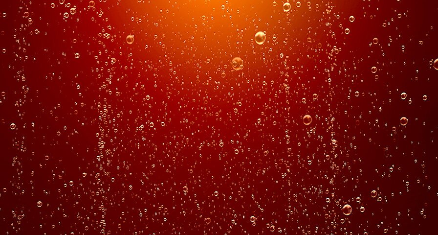 Blasen steigen in einer rot-orangefarbenen  Flüssigkeit auf.