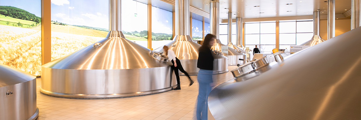 Sudhaus der Krombacher Brauerei mit großen Edelstahl-Braukesseln und Mitarbeitenden im Hintergrund.