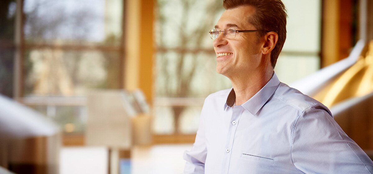 Mann in einem hellblauen Hemd steht in einer Brauerei mit großen Braukesseln im Hintergrund.