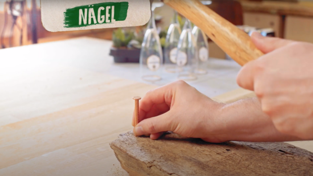 Nägel werden mit einem Hammer in das Holzstück angebracht.