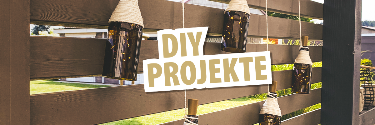 Fünf hängende Flaschen mit Schnur an einer Holzlattenwand. Der Text 'DIY PROJEKTE' ist in großen, hellen Buchstaben über dem Bild platziert.