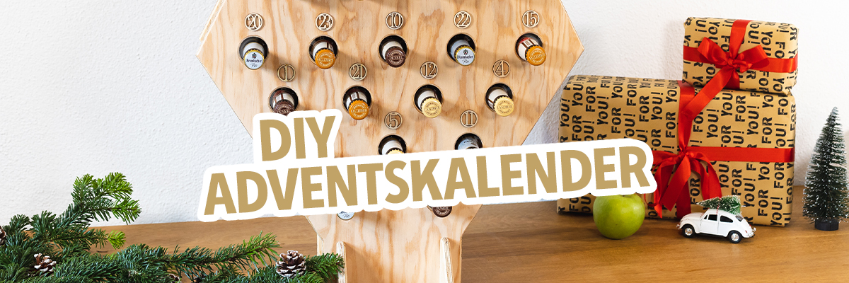 Ein DIY-Adventskalender in Form eines Weihnachtsbaums aus Holz mit 24 Kapseln. Im Hintergrund sind Geschenke und eine grüne Apfel sichtbar.