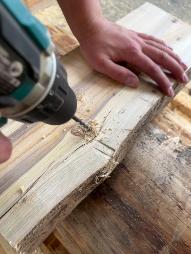 Ein Handwerker benutzt einen Winkelschleifer, um Holz zu bearbeiten. Der Fokus liegt auf der Schleifmaschine und dem bearbeiteten Holzstück.