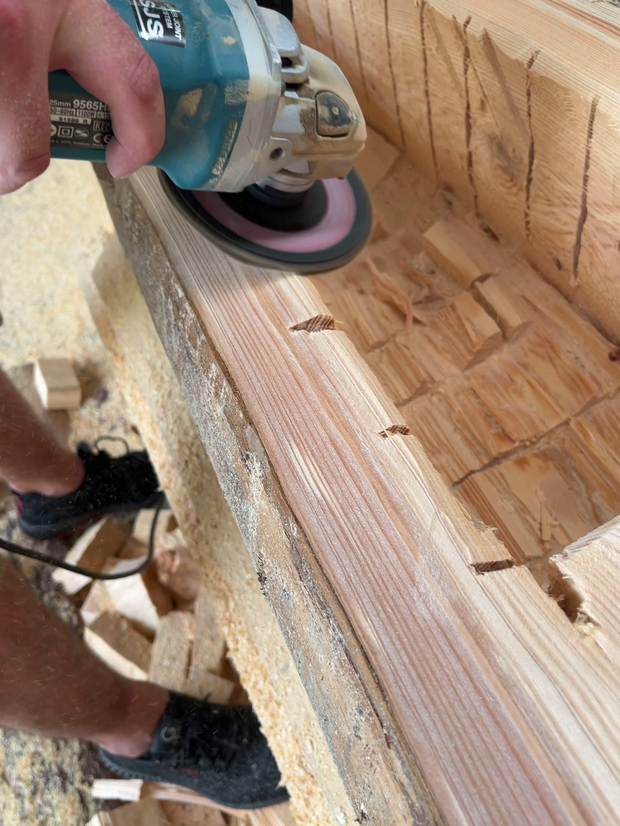 Ein Handwerker benutzt einen Winkelschleifer, um Holz zu bearbeiten. Der Fokus liegt auf der Schleifmaschine und dem bearbeiteten Holzstück.