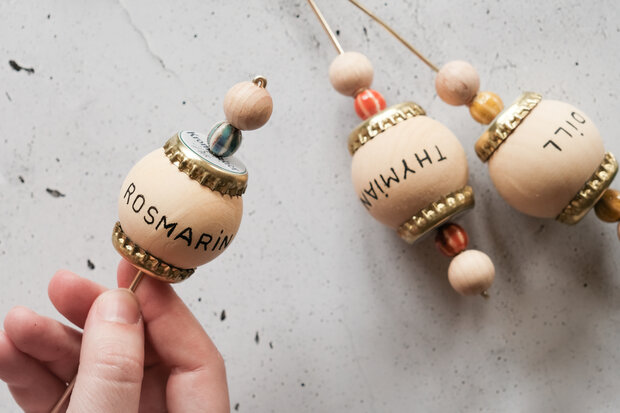 Holzkugel sind mit Perlen und Kronkorken auf Holzstab gesteckt.