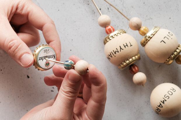 Auf ein Holzspieß werden Perlen und ein Kronkorken aufgespießt.