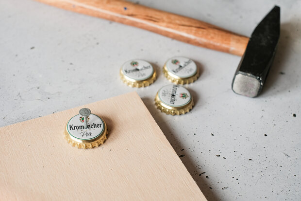 Mit einem Hammer und einem Nagel wird ein Loch in ein Kronkorken gehauen.