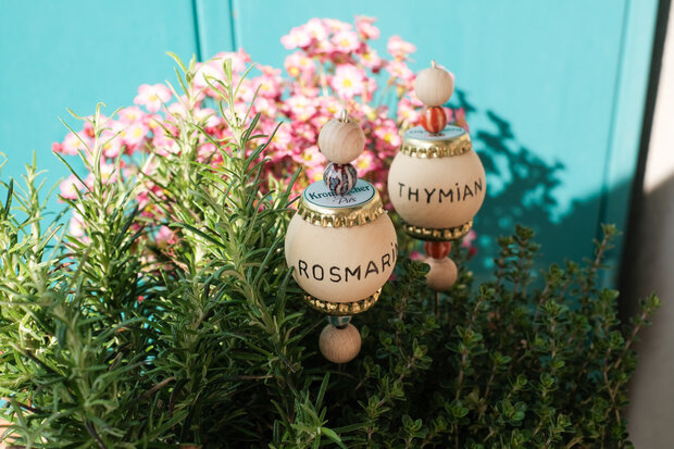Fertige Beetbeschriftung auf Holzkugeln in einer Rosmarinpflanze.