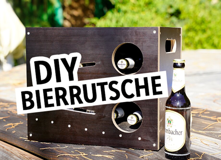 Ein schwarzes Holzgestell mit zwei runden Ausschnitten, in denen Flaschen stehen. Daneben eine Bierflasche von 'Krombacher'. Der Text 'DIY BIERRUTSCHE' ist in großen, weißen Buchstaben auf schwarzem Hintergrund zu sehen.