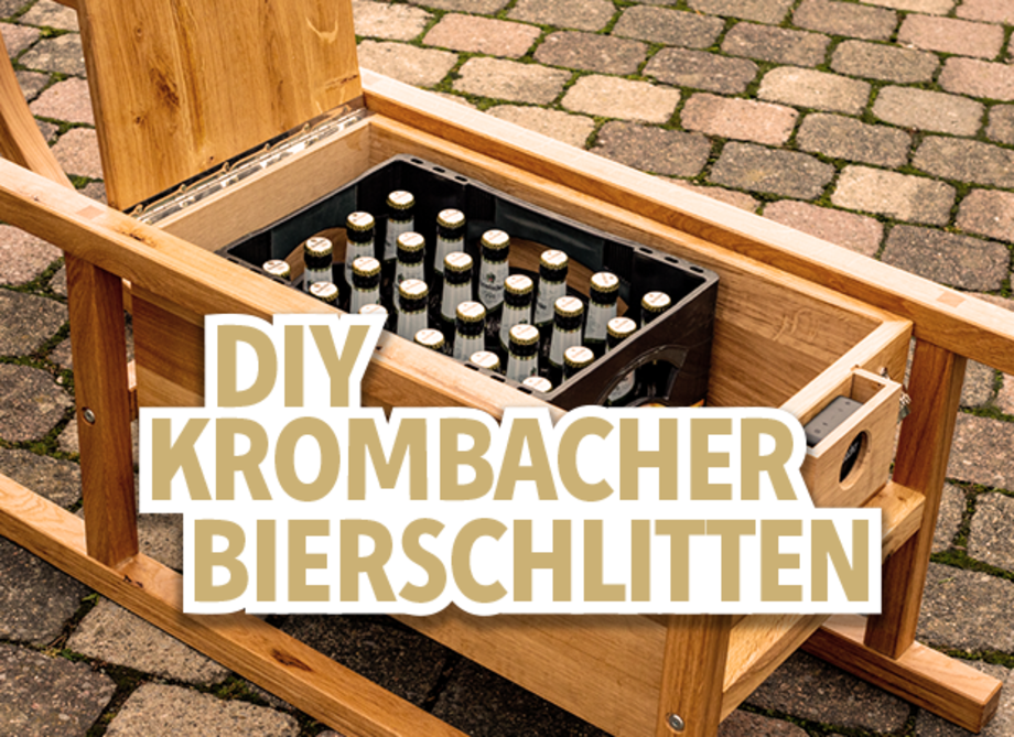 Ein Holzstuhl mit einem offenen Fach, das eine Kiste mit Flaschen enthält. Darauf steht der Text 'DIY Krombacher Bierschlitten'.