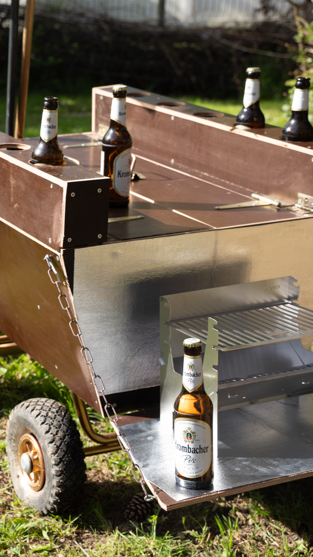 Fünf Krombacher Pilsflaschen stehen auf einem bierwagen aus Holz.