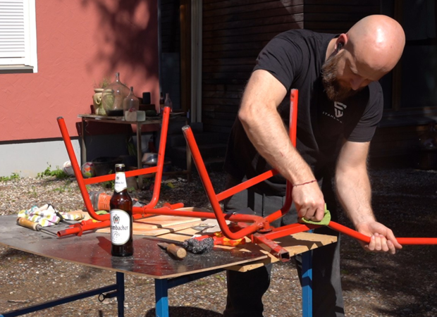Ein Mann zerlegt einen Bollerwagen in Einzelteile auf einem Tisch und eine Bierflasche steht daneben.