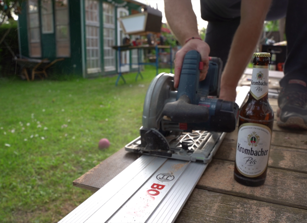 Siebdruckplatten werden mit einer Handkreissäge ausgeschnitten. Eine Krombacher Pils Flasche steht daneben.