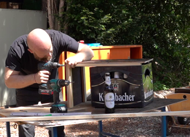 Aus zwei Siebdruckplatten werden Sitzbänke mit Krombacher Kisten gebaut und zusammengeschraubt.