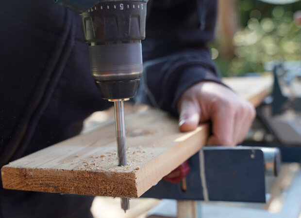 In ein Holzbrett werden Löcher gebohrt.
