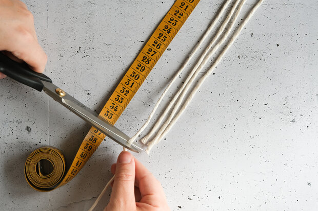 Eine Person schneidet mit einer Schere mehrere Schnüre, die auf einem Maßband liegen. Das Maßband zeigt Zahlen von 1 bis 36.