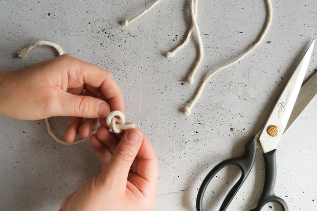 Eine Person bindet einen Knoten in ein Stück weißen Stoffband. Neben der Person liegen eine Schere und mehrere lose Enden des Bandes.
