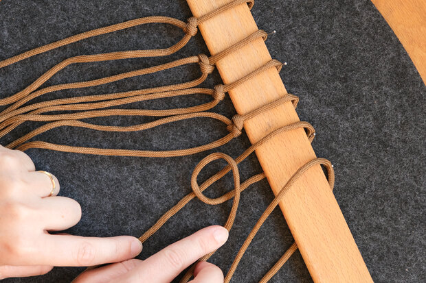 Braune Seile werden an ein Holzstab geknotet.