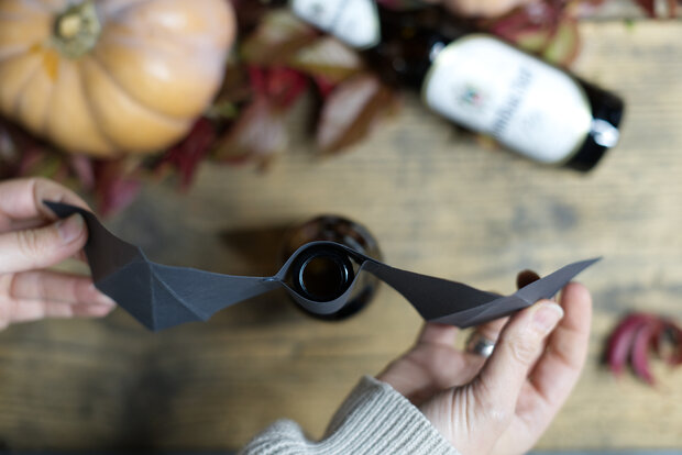 Der schwarze Papierfledermausflügel wird an einen Flaschenhals befestigt.