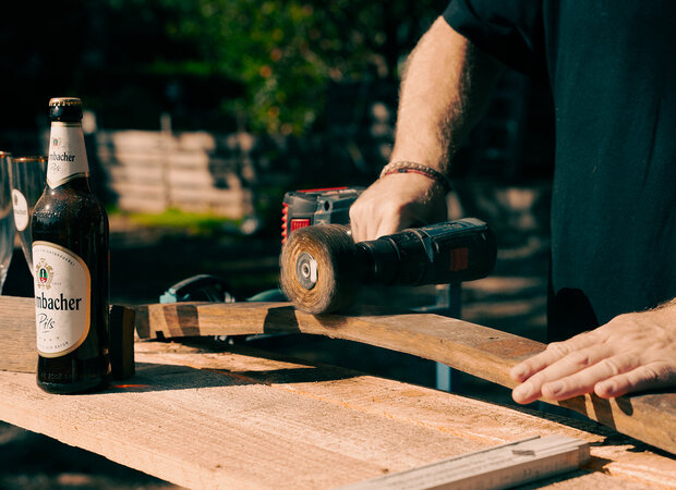 Ein Holzbrett wird gebürstet und eine Krombacher Pilsflasche steht auf dem Tisch.