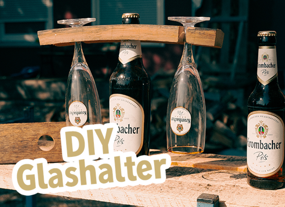 Eine Pilsflasche trägt am Flaschenhals ein Holzstück mit zwei Krombacher Pils Gläsern und Text: DIY Glashalter.