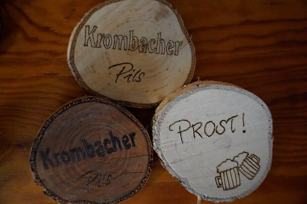 Drei runde Krombacher Holzuntersetzer mit Text: Prost und Krombacher Pils.