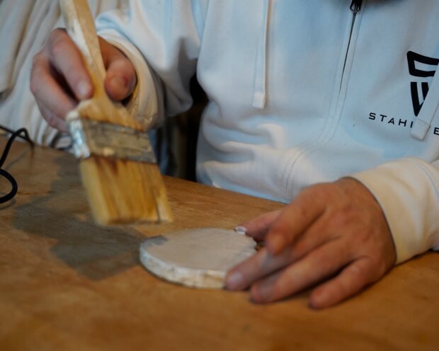 Holzscheiben werden mit einem Pinsel bestrichen.