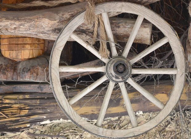 Altes Wagenrad steht an Holzstapel.