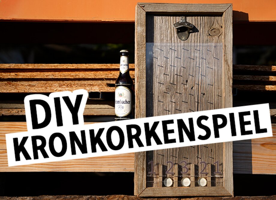 Ein Holzrahmen mit einem DIY Kronkorkenspiel, das mit Nägeln und Zahlen von 1 bis 5 versehen ist. Neben dem Spiel steht eine Flasche Bier von der Marke 'Lächer'.