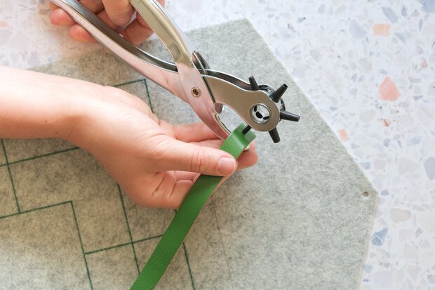 In ein grünes Lederband werden Löcher reingestanzt.