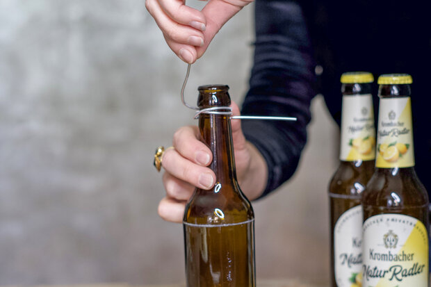 Eine leere braune Flasche wird mit einem Draht am Flaschenhals umwickelt.