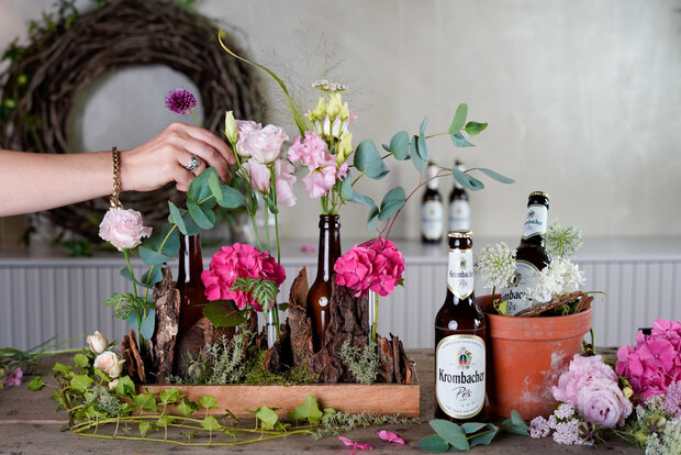 In die mit Wasser befüllten braunen Glasflaschen werden Blumen platziert.